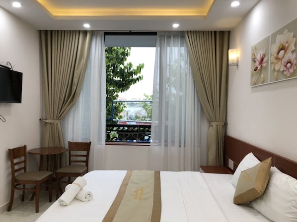 Habitación de hotel con cama, escritorio, sillas, ventana con cortinas, televisor montado en la pared y una obra de arte floral.