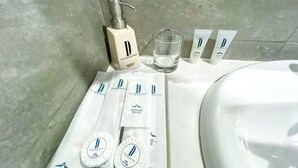 Un baño con un lavamanos blanco, una botella de loción, un vaso de agua y varios tubos de crema.