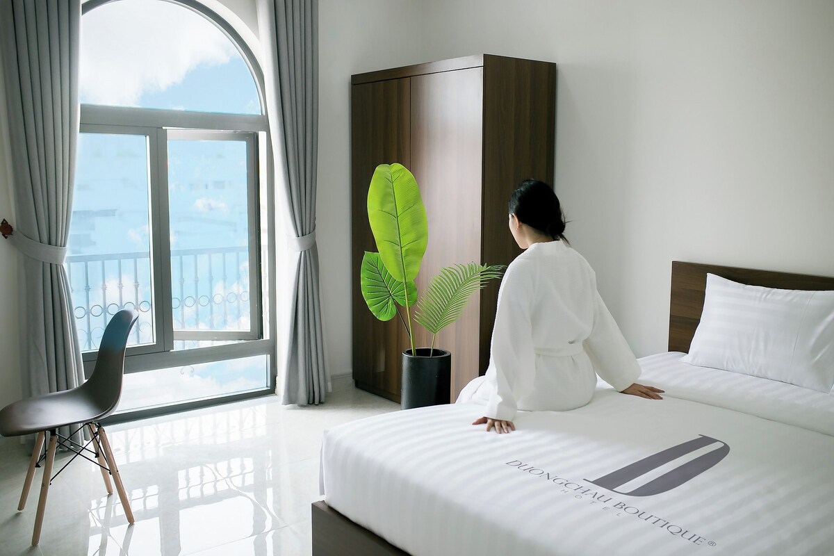 A hotel room with a bed, a potted plant, a chair, and a wardrobe.