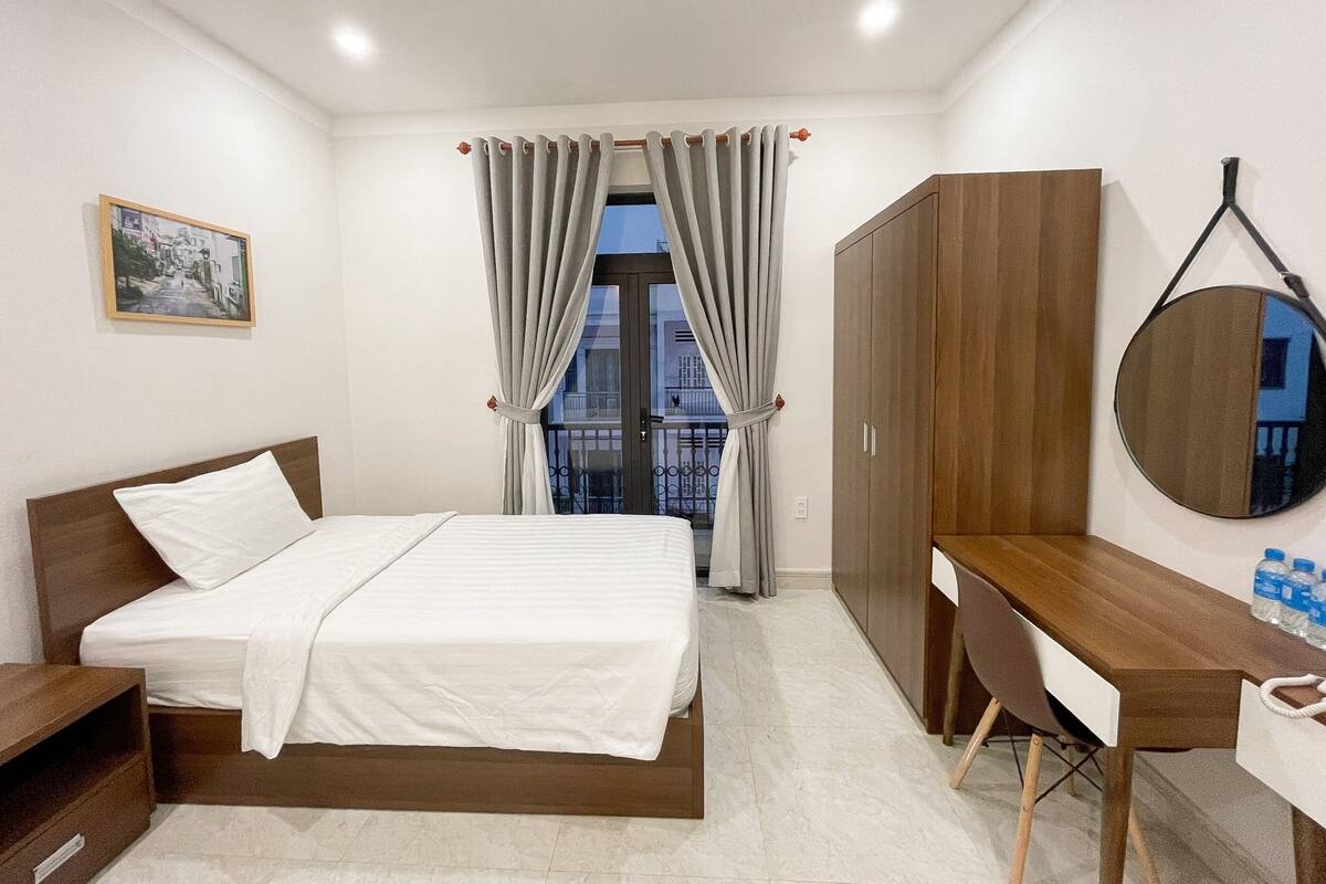 A bedroom with a bed, a desk, a wardrobe, and a window with curtains.