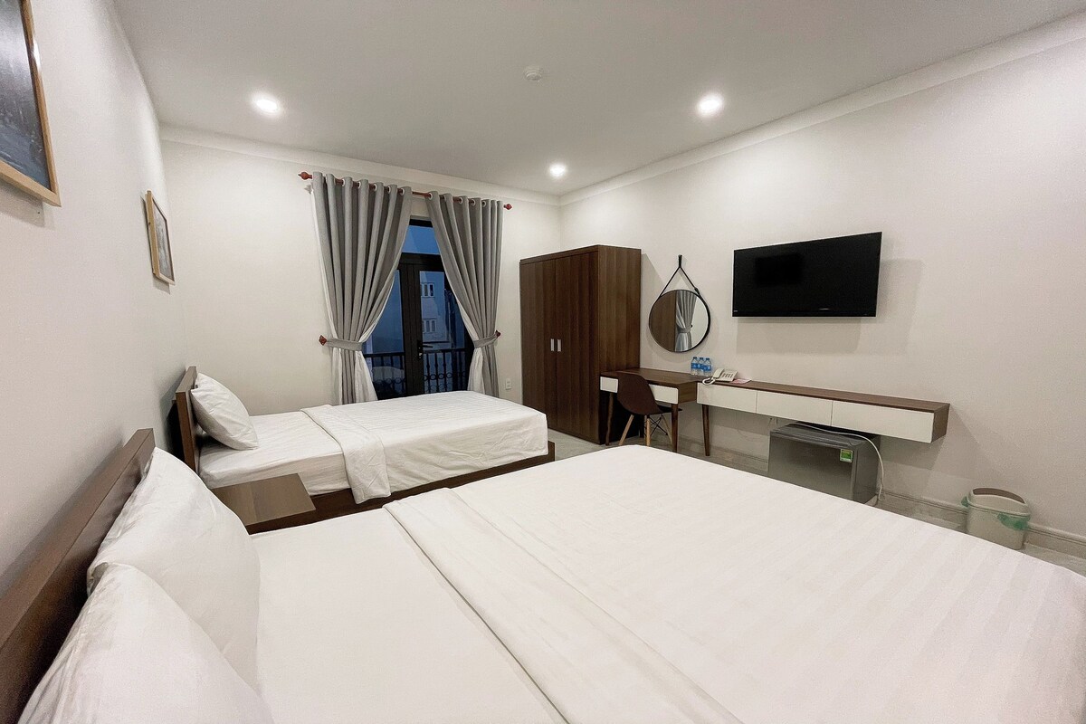 A hotel room with two beds, a desk, a chair, a TV, and a window with curtains.