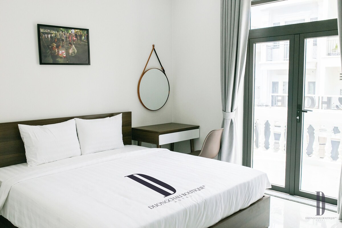 A hotel room with a bed, a bedside table, a mirror, and a window with curtains.