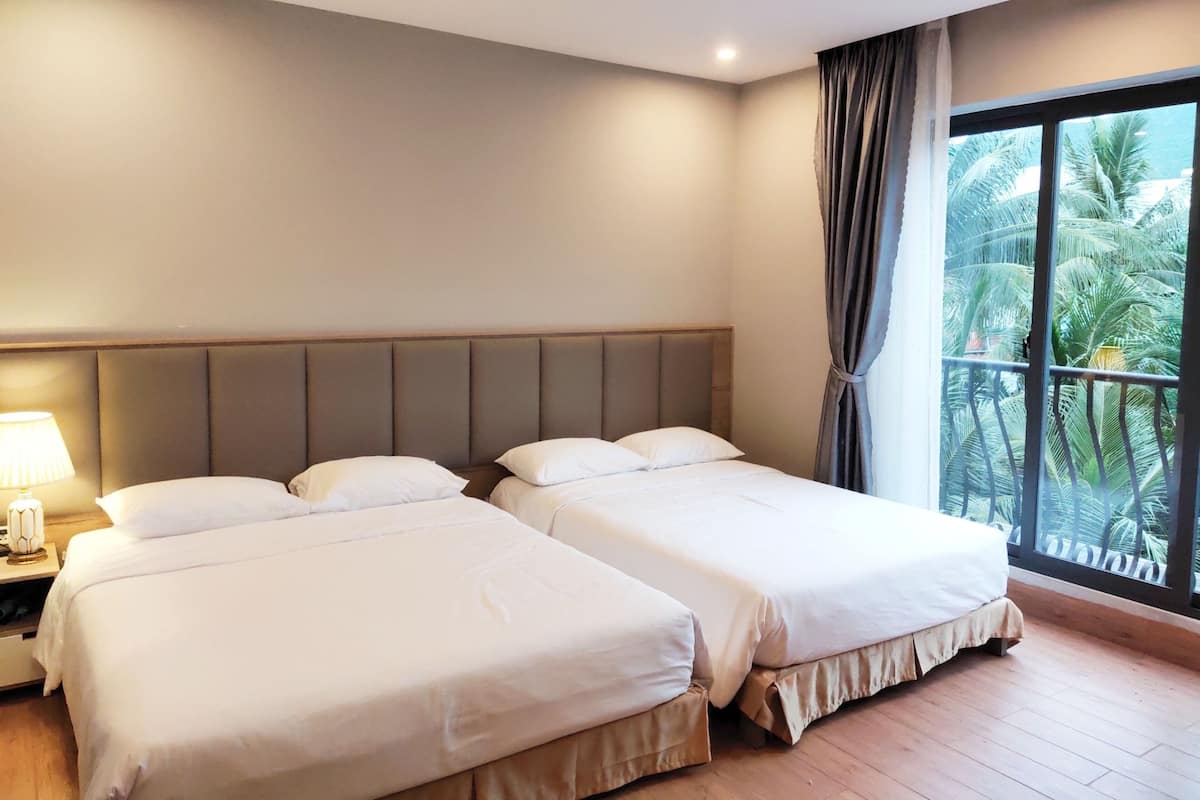 A hotel room with two beds, a nightstand, a lamp, and a large window with a view of palm trees.