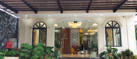 A hotel entrance with a modern design, featuring a large sign above the entrance, a glass door, and potted plants around the entrance area.