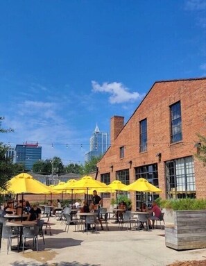 Relax in the outdoor seating area with tables and chairs under shaded umbrellas, surrounded by the city's modern skyline.