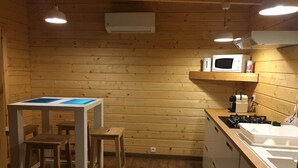 Una cocina compacta con paredes de madera, una pequeña mesa de comedor, taburetes, microondas, cocina a gas y un lavamanos.
