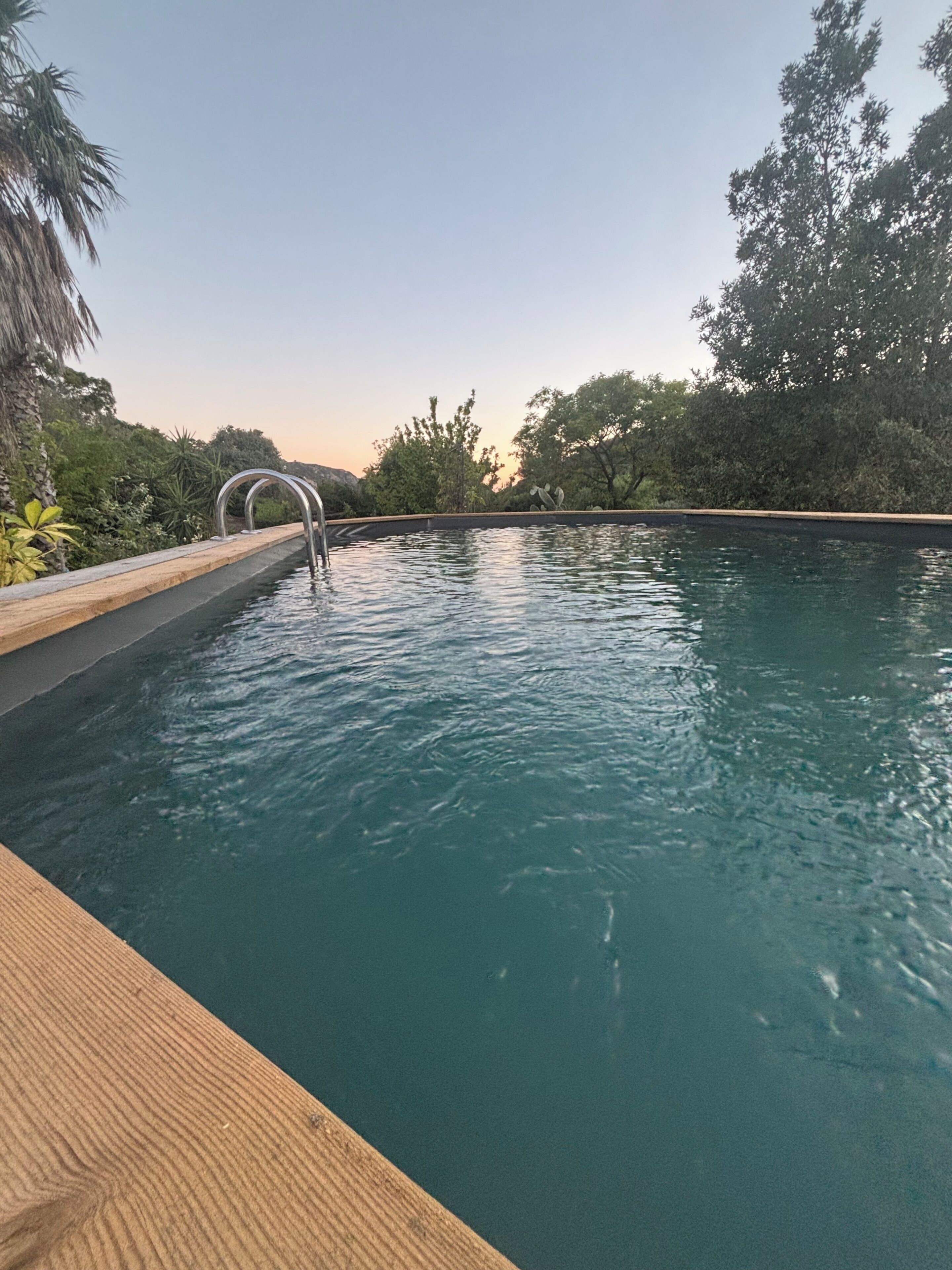 A swimming pool with a wooden deck and metal handrail.