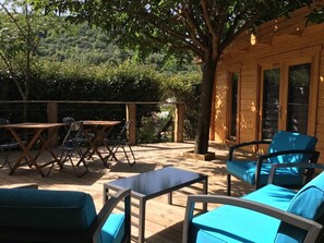 Une terrasse en bois avec des meubles d’extérieur, notamment une table et des chaises, et un bâtiment en bois doté de grandes fenêtres.