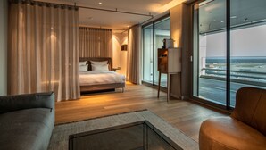 A modern hotel room with a large bed, a sofa, a small table, and a view of the airport. - b'mine Frankfurt Airport, WorldHotels Crafted (Frankfurt)