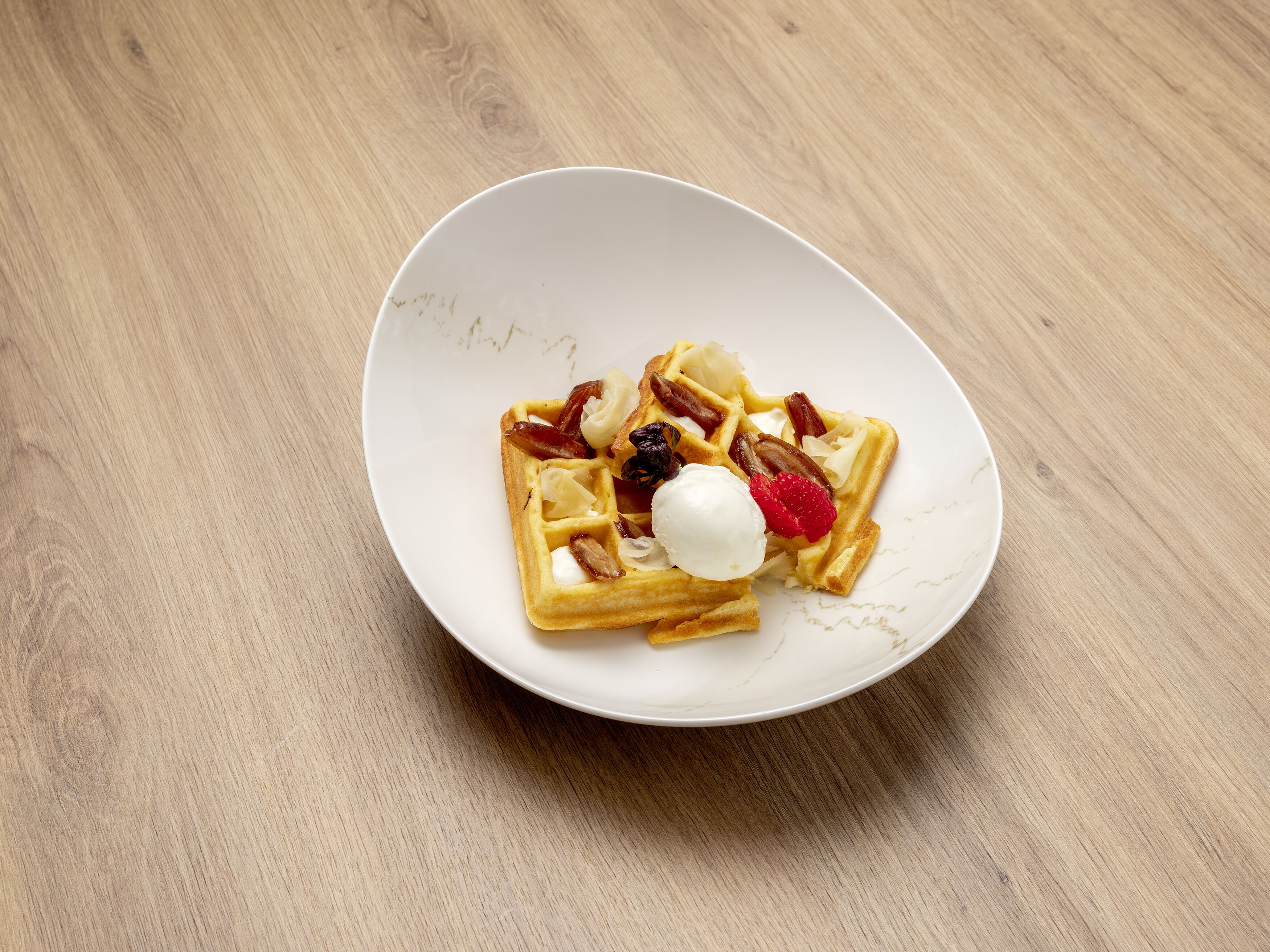 A white plate with waffles, fruit, and a scoop of ice cream on a wooden table.