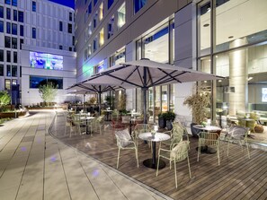An outdoor dining area with tables and chairs, large umbrellas, and potted plants. - b'mine Frankfurt Airport, WorldHotels Crafted (Frankfurt)