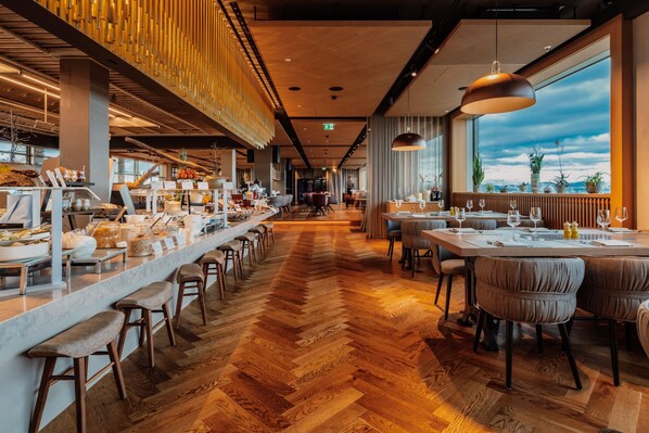 A modern restaurant with a long counter, bar stools, and a herringbone wood floor.