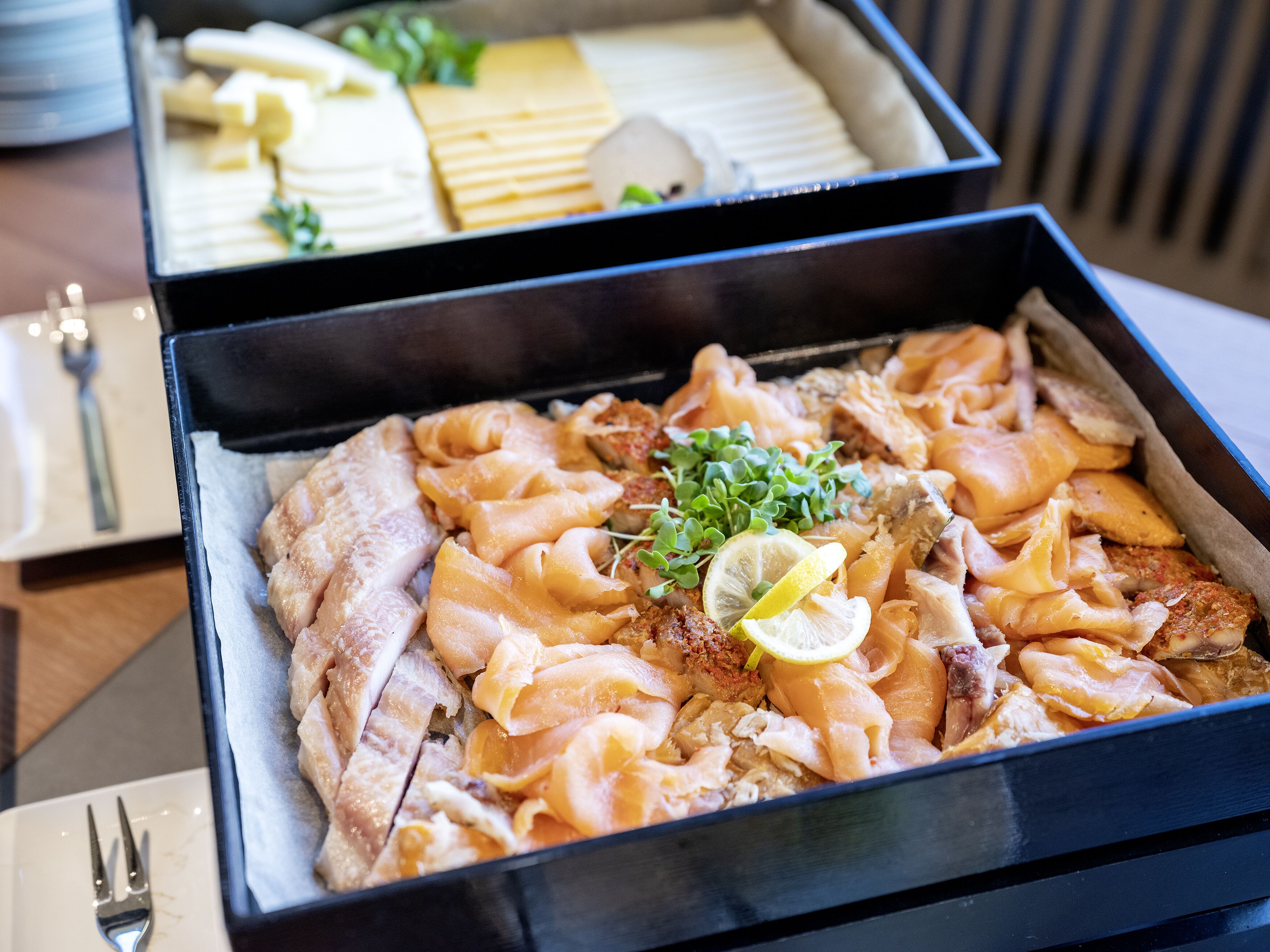 A tray of assorted seafood including fish and possibly crab, garnished with lemon and greens, in a black tray.