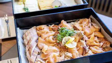 A tray of assorted seafood including fish and possibly crab, garnished with lemon and greens, in a black tray.