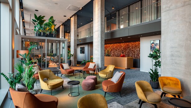 A spacious lobby with multiple seating areas, a reception desk, and a large plant display. - b'mine Frankfurt Airport, WorldHotels Crafted (Frankfurt)