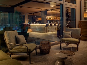 A modern outdoor seating area with wicker furniture, a bar in the background, and a view of the cityscape. - b'mine Frankfurt Airport, WorldHotels Crafted (Frankfurt)