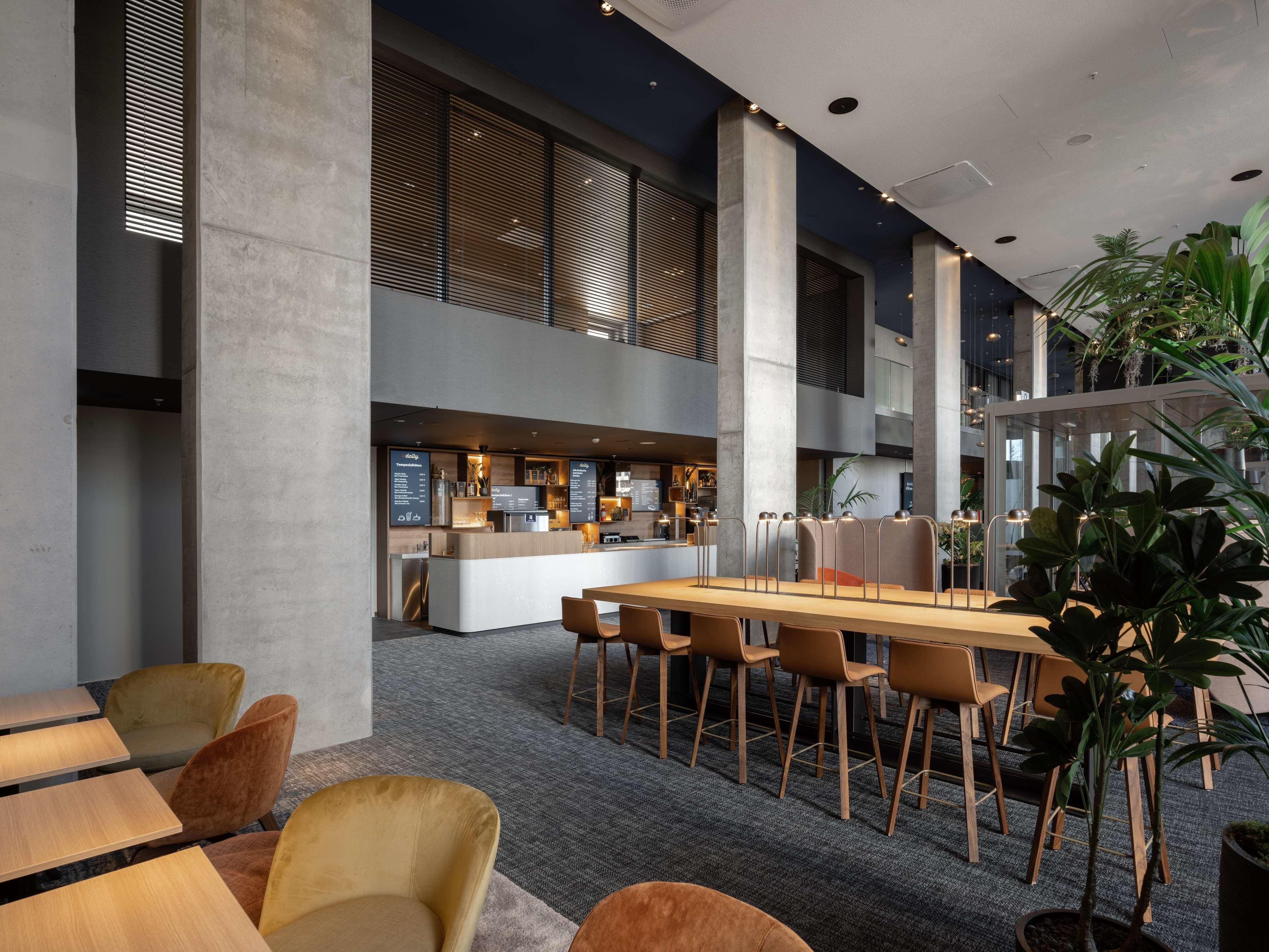 Un espacio interior moderno con una zona de comedor central, diferentes disposiciones de asientos y una barra.
