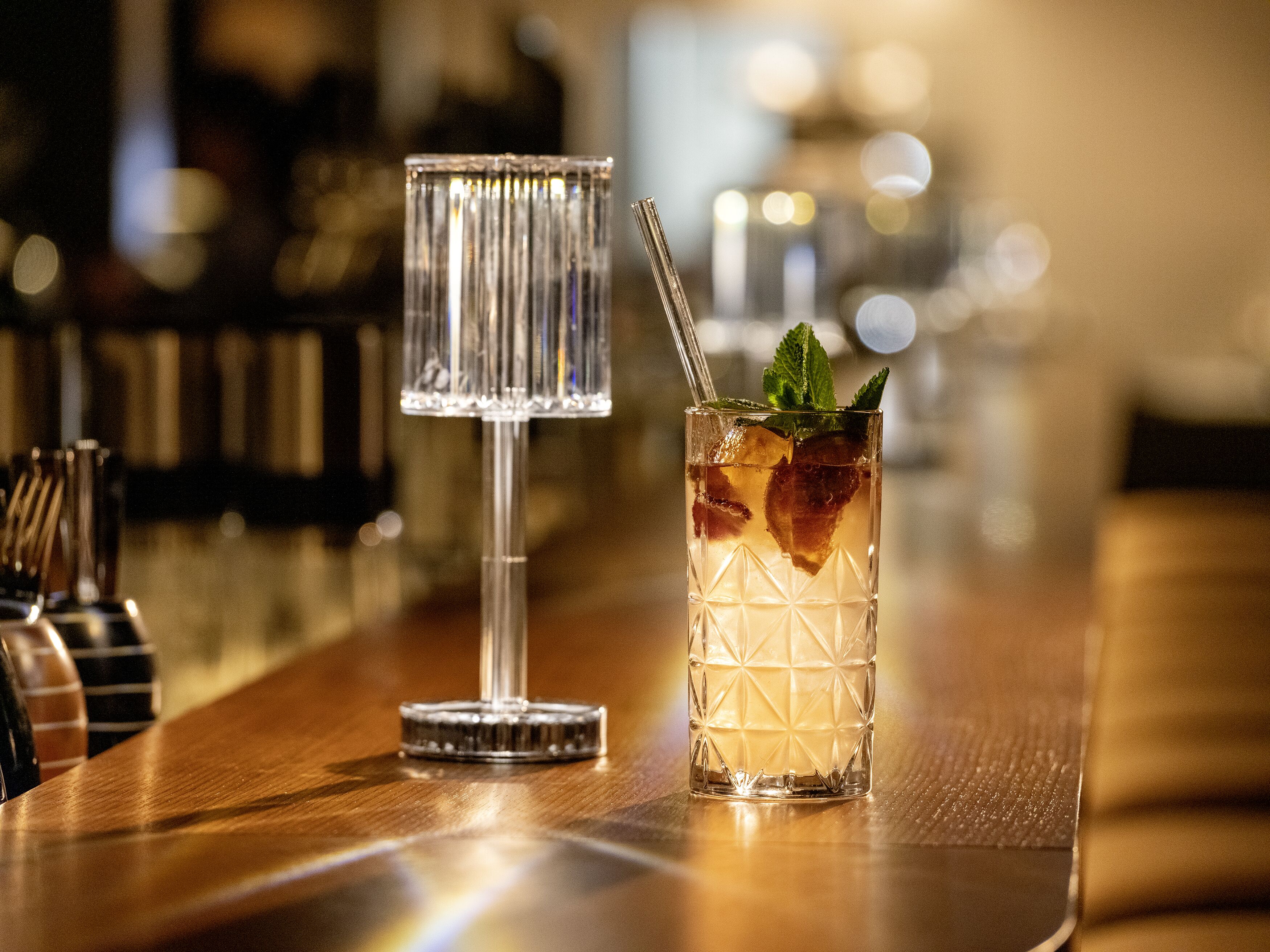 A bar setting with a clear glass and a tall glass with ice and a straw.