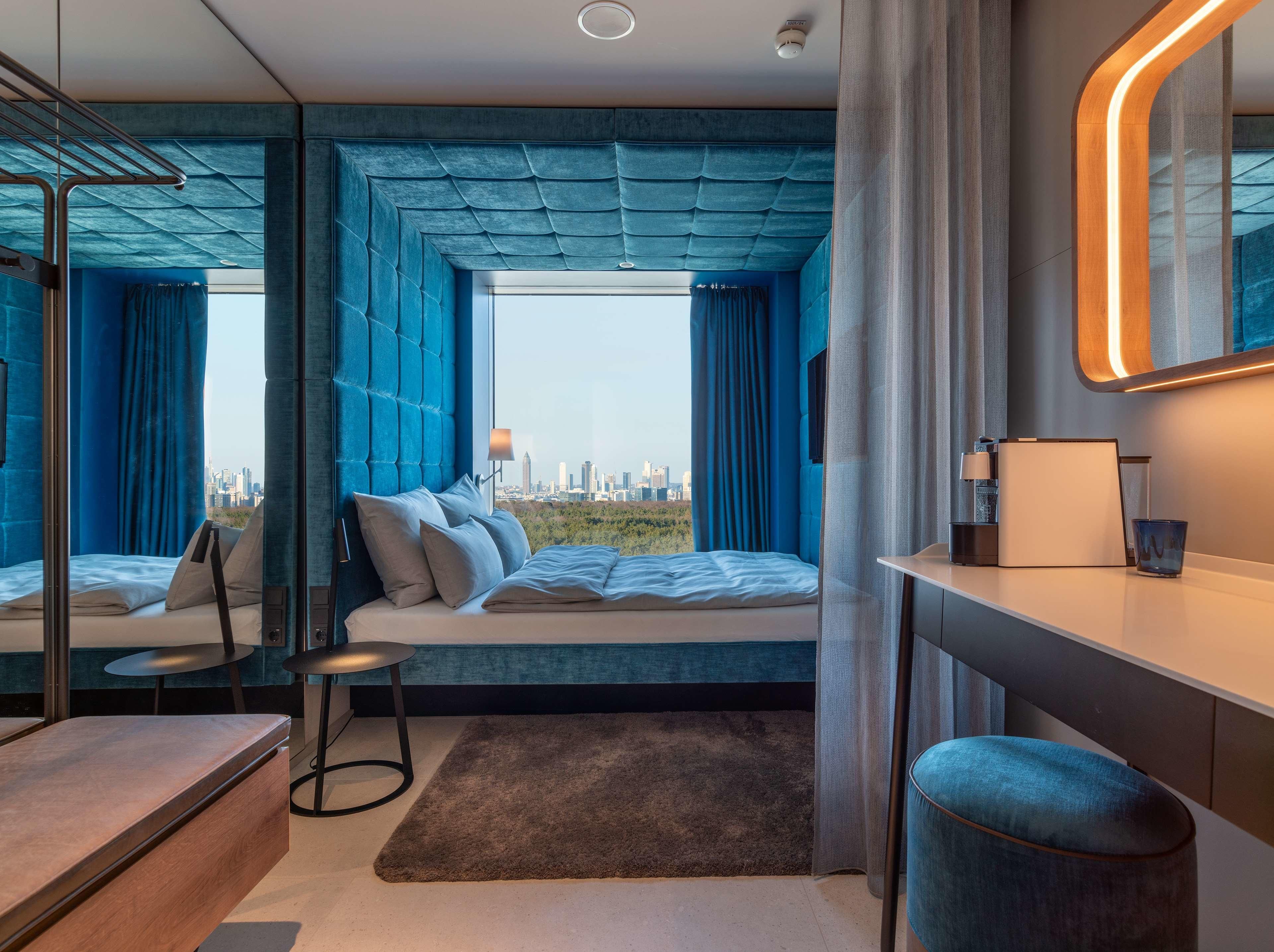 Un dormitorio moderno con vistas a la ciudad, una cama con almohadas, un escritorio con lámpara y una silla.
