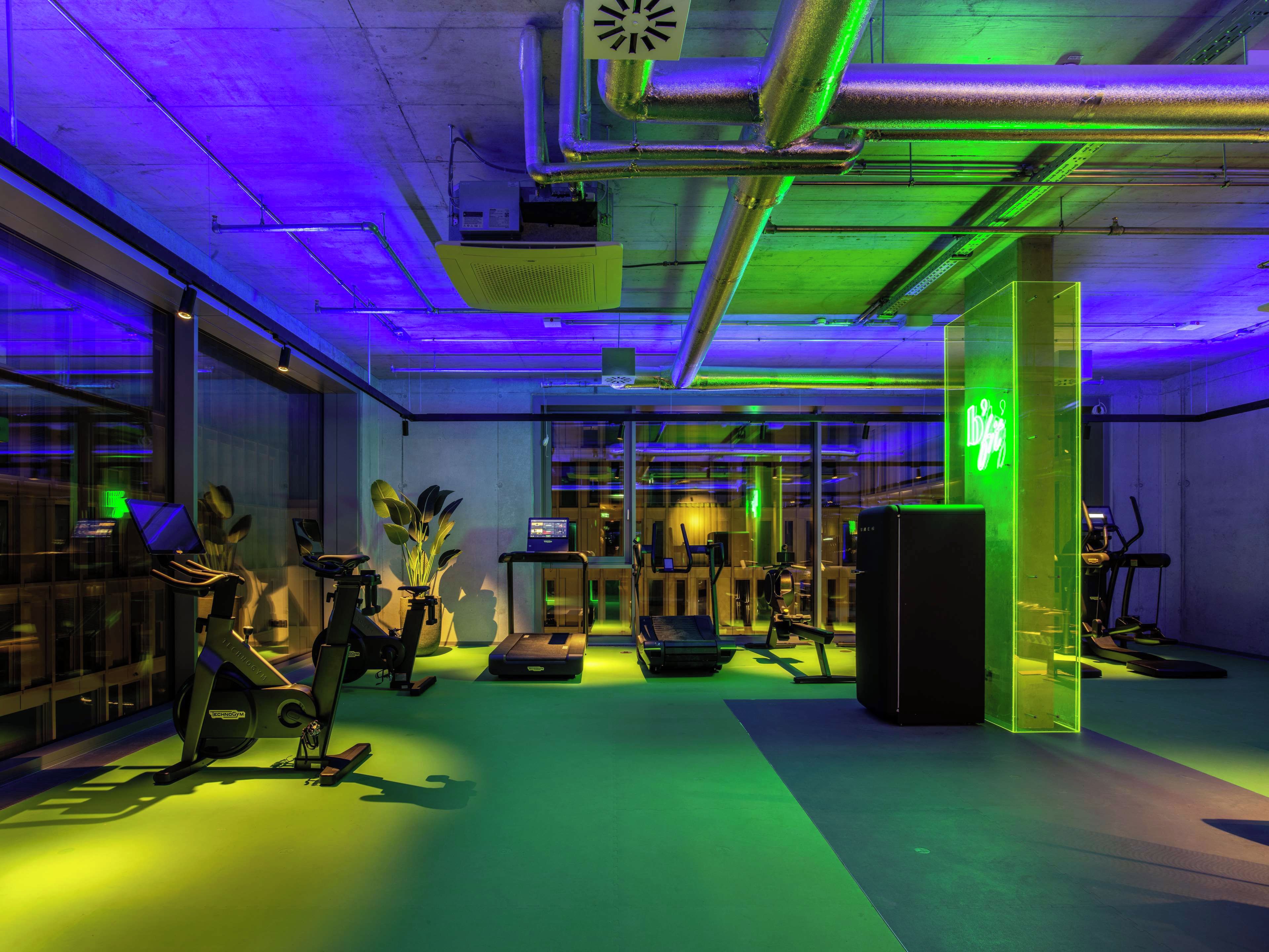 A modern gym with exercise equipment, a reception desk, and a neon sign.