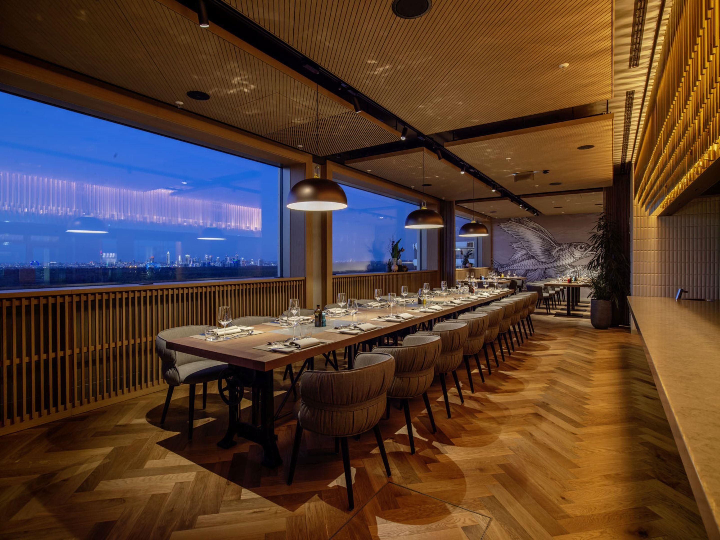 Una larga mesa de comedor con sillas, vista a la ciudad y un diseño interior moderno.