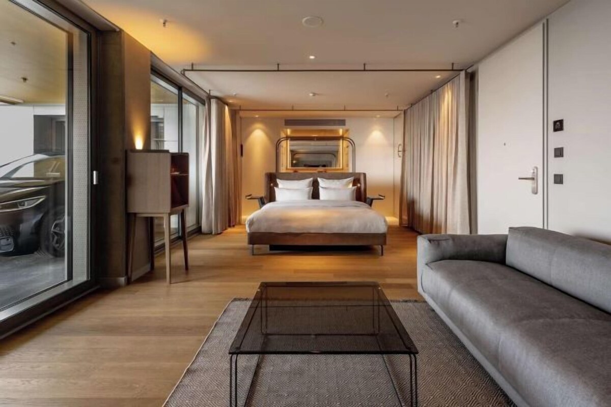 Habitación de hotel moderna con una cama grande, un sofá, un televisor y vistas a través de un ventanal corredero.
