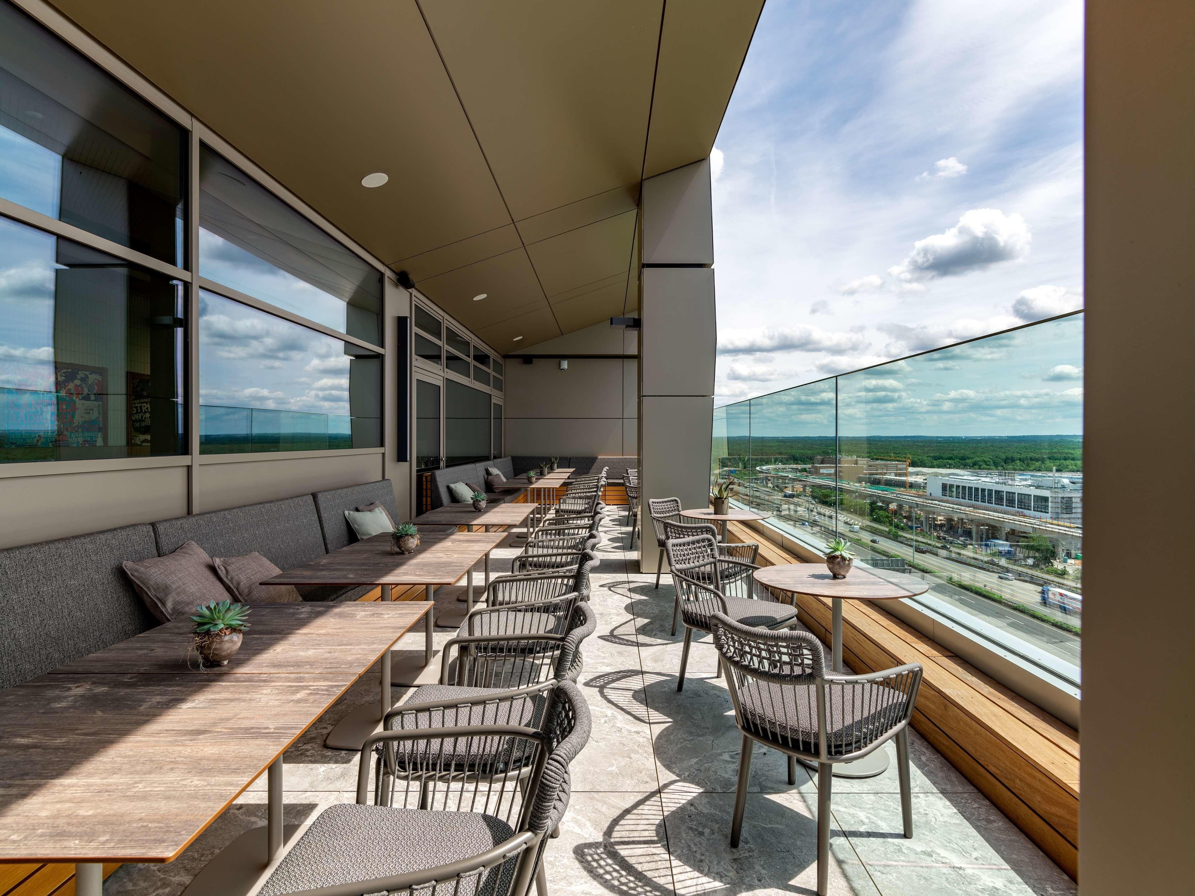 A modern outdoor seating area with tables and chairs, large windows, and a view of a highway.
