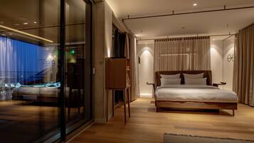 A modern hotel room with a large bed, a glass wall, and a view of the city at night.