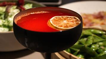 A table with a red drink in a glass, a bowl of green vegetables, and a plate of food in the background.