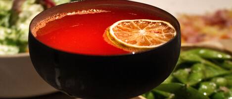A table with a red drink in a glass, a bowl of green vegetables, and a plate of food in the background.