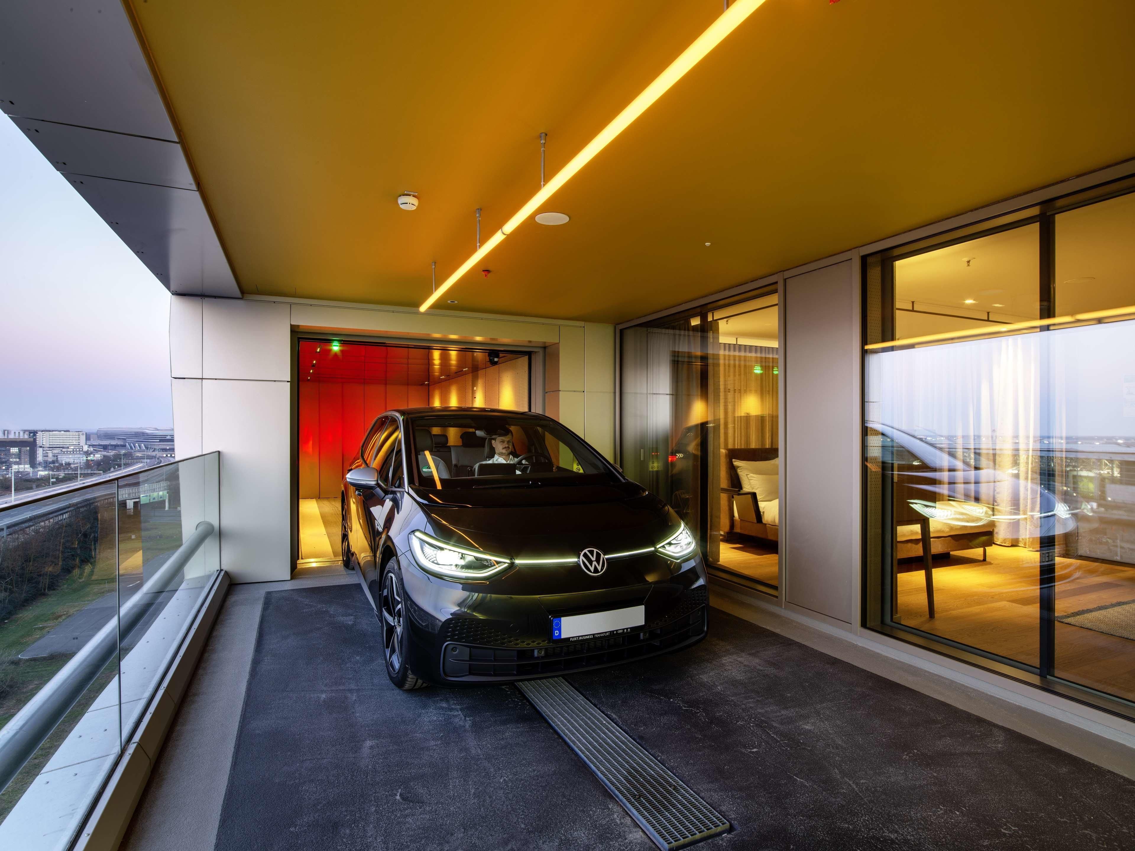 A modern hotel room with a large window, a balcony, and a parked car.