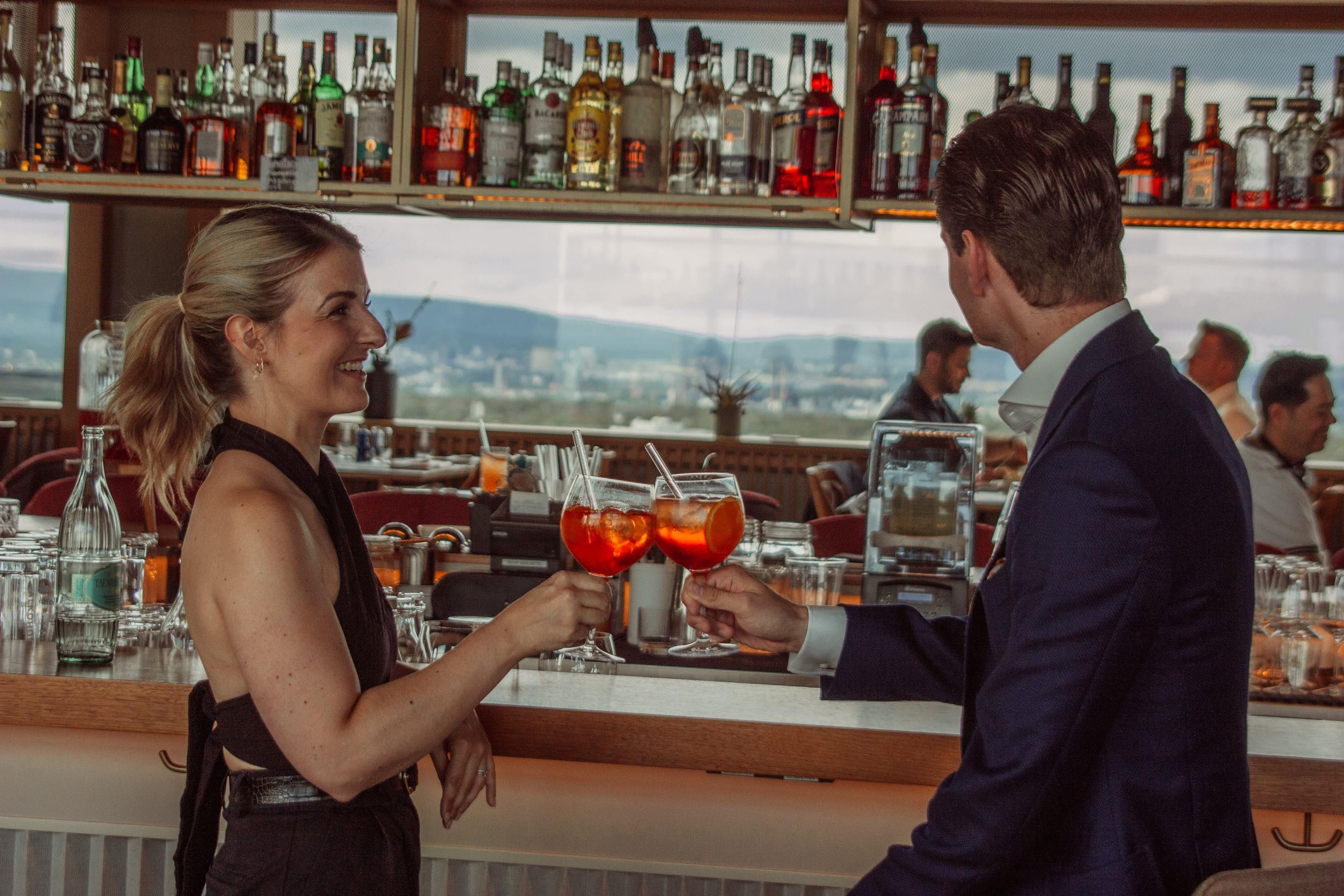 A bar with a bartender and a customer holding drinks.