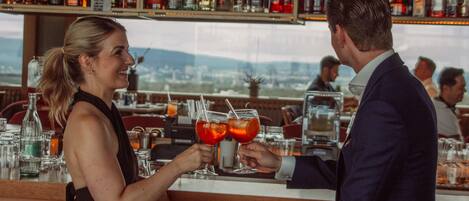 A bar with a bartender and a customer holding drinks.