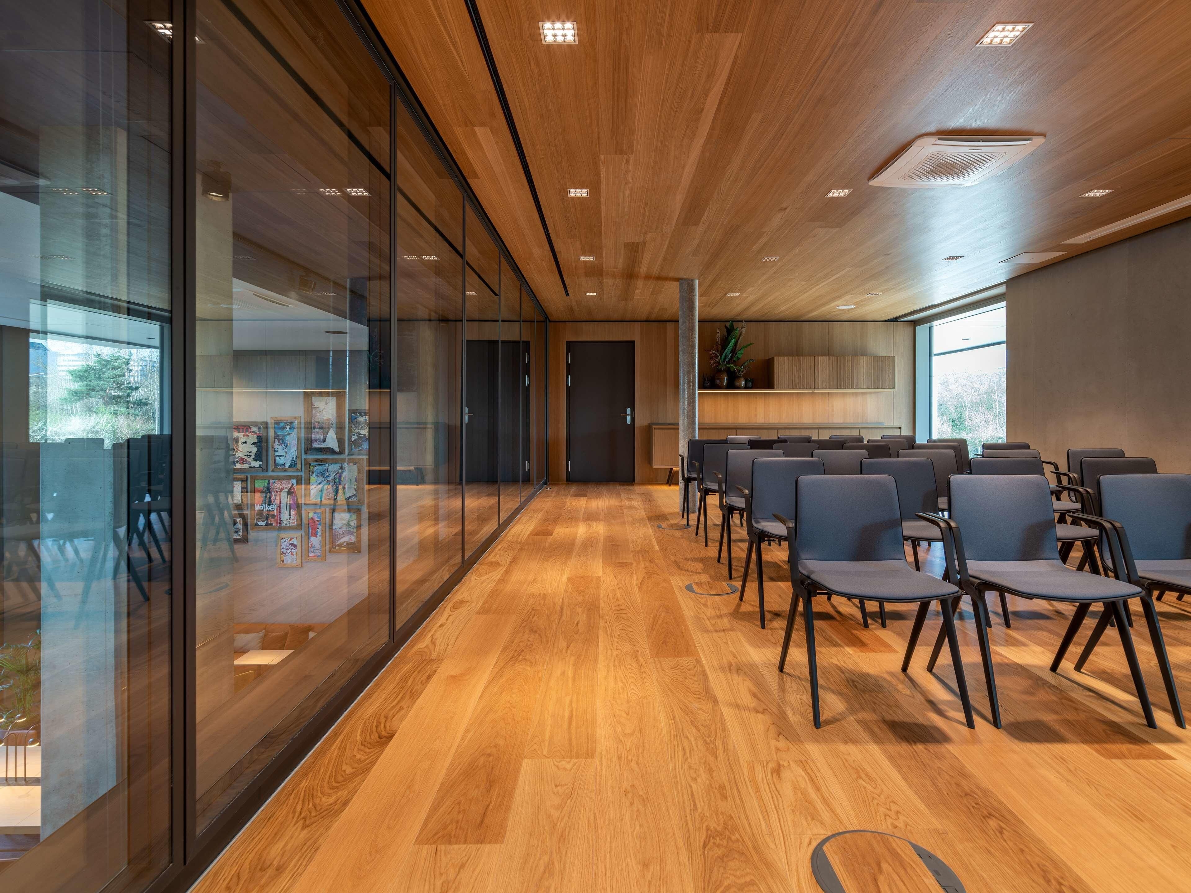 A conference room with glass walls, wooden flooring, and rows of chairs.