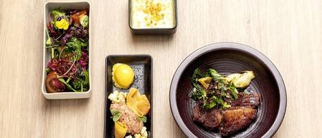 A wooden table with three dishes: a salad, a small bowl of soup, and a plate with meat and vegetables.