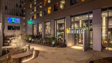 A modern hotel exterior at night with illuminated windows, outdoor seating, and a well-lit entrance.
