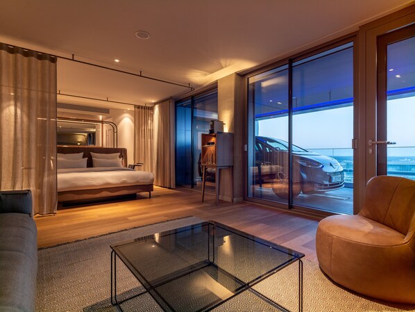 A modern hotel room with a large bed, a glass partition, a seating area, and a view of a cityscape. - b'mine Frankfurt Airport, WorldHotels Crafted (Frankfurt)