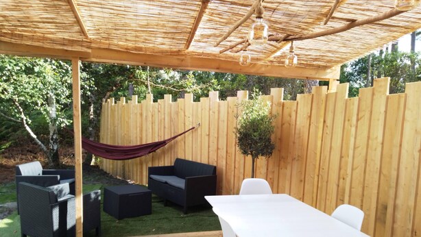 A covered patio with a wooden deck, outdoor furniture, and a hammock. - Studio in the pines (Lacanau)