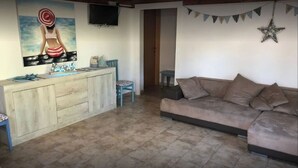 A living room with a sofa, a small table, and a TV mounted on the wall. - Cottage a few steps from the sea (Gallina)