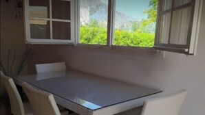 A dining area with a table and four chairs, a window with a view of greenery, and a partially open door. - Cottage a few steps from the sea (Gallina)
