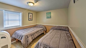 Quarto pequeno, com uma cama de casal, ventoinha no teto, aquecedor e janela com cortinas.