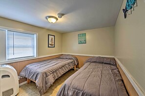 A small, single-room with two beds, a ceiling fan, a heater, and a window with blinds.
