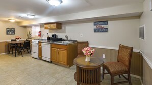 Cozinha compacta com armários de madeira, pia e fogão. Há uma área de refeições com mesa e cadeiras, e um letreiro decorativo na parede.