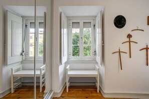 A room with a white bench, a window with shutters, and a wall with a hat and hangers.
