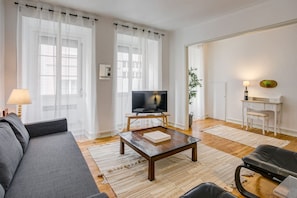 A living room with a sofa, a coffee table, a TV on a stand, a desk, and a chair.