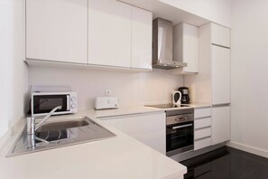 A modern kitchen with white cabinets, a microwave, toaster, coffee maker, and an oven.