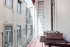 A balcony with a metal railing, a wooden table, and a wicker basket with flowers.