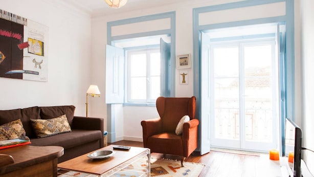 Una sala de estar con un sofá marrón, una mesa de centro de madera, un sillón rojo y un televisor sobre un mueble.