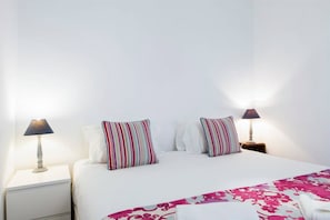 A neatly made bed with striped pillows, a white headboard, and a pink floral bedspread.