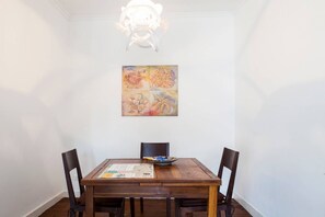 Un comedor con una mesa de madera, cuatro sillas, un cuadro en la pared y una araña.
